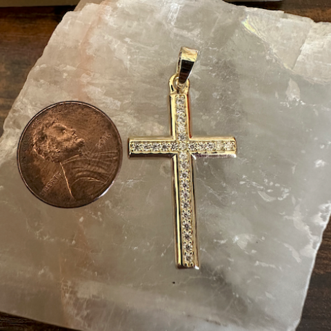 Gold cross pendant with clear stones on a rock next to a coin for scale.