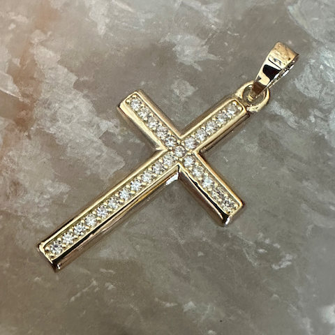 Gold cross pendant with diamonds on a stone surface