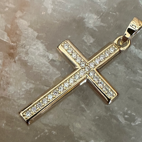 Gold cross pendant with clear stones on a marble surface