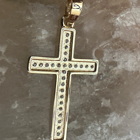 Gold cross pendant with embedded stones on a marble surface