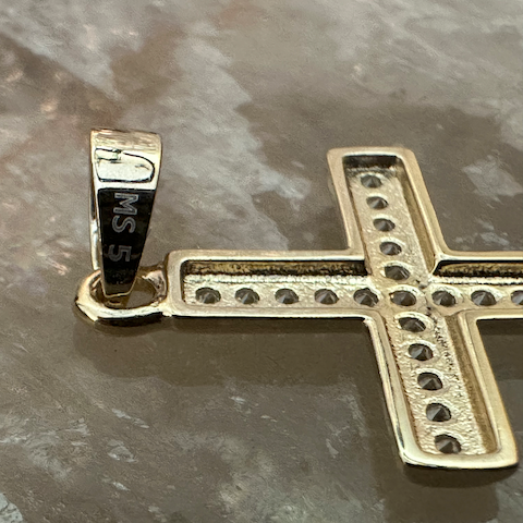 Gold cross pendant with engraved text on a reflective surface