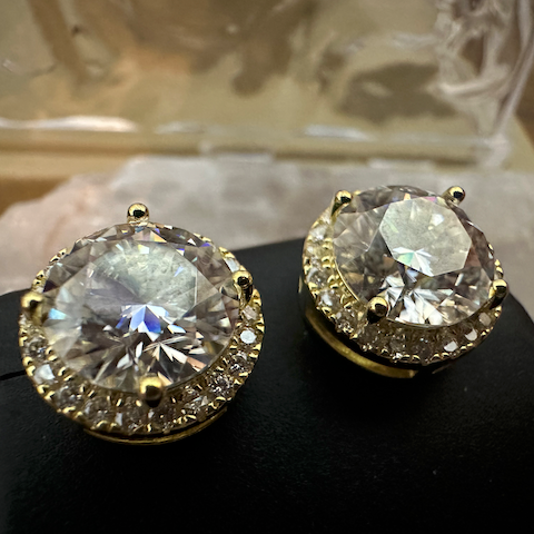 Pair of gold and crystal stud earrings on a black stand with a blurred background.