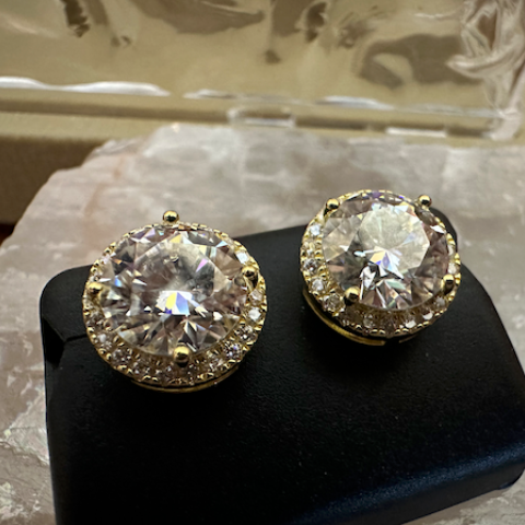 Pair of gold and crystal earrings on a black stand with a textured surface background.