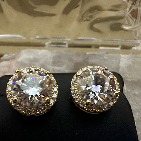 Pair of gold and diamond stud earrings on a black stand with a reflective surface in the background.