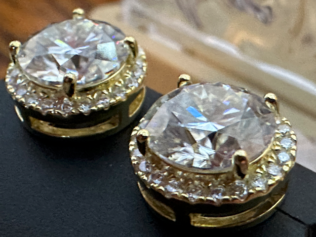 Gold earrings with large central gemstones on a dark surface