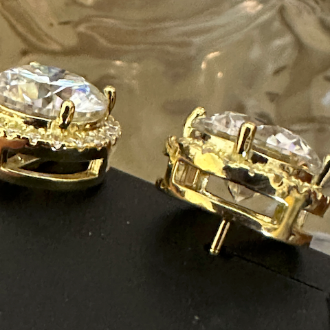 Gold earrings with clear gemstones on a reflective surface