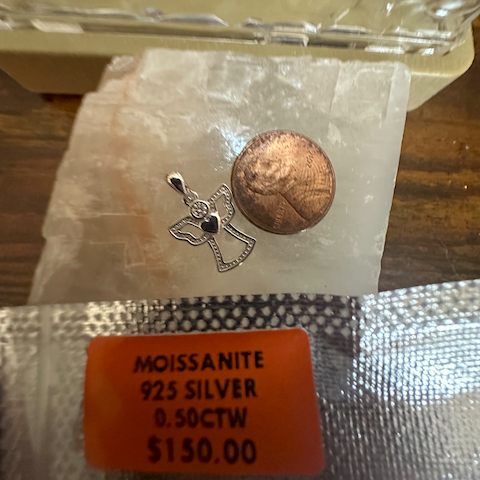 Jewelry with a label indicating 'Moissanite 925 Silver 0.50CTW $130.00' on a reflective surface.