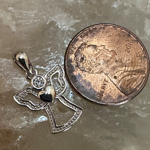 Small silver cross pendant with a black stone next to a penny on a textured surface