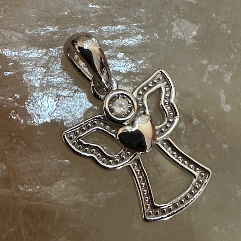 Silver cross pendant with a small black heart and clear gemstone on a reflective surface.