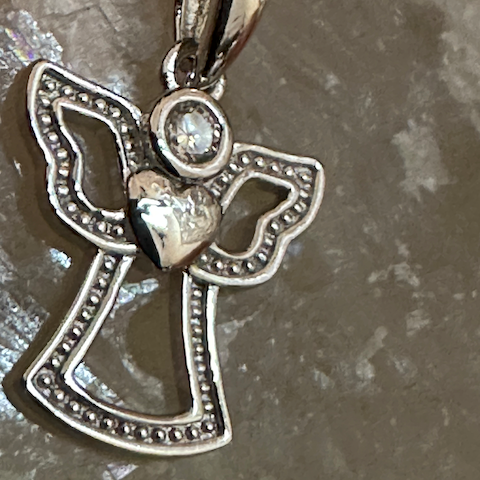 Silver angel pendant with a heart and clear gemstone on a textured gray background