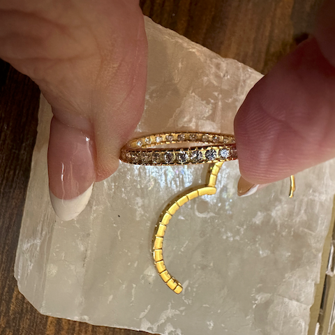 Gold bracelet with embedded stones held by a hand on a clear stone surface.