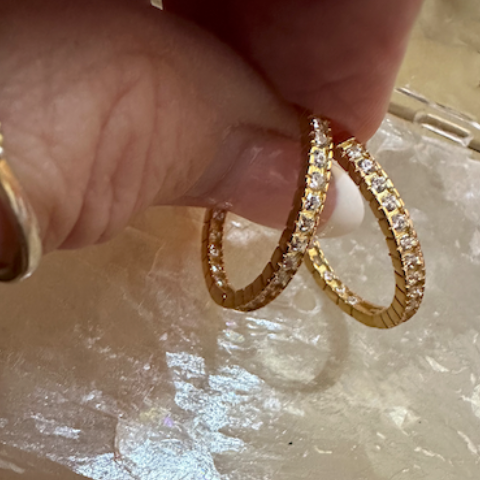 Gold hoop earrings held by a hand on a crystal surface