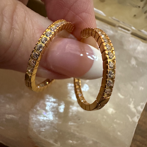 Gold hoop earrings with embedded stones held by a hand on a light background