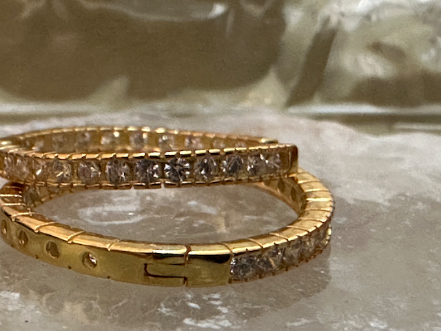 Two gold bracelets with diamond accents on a reflective surface