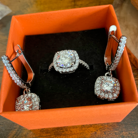 Silver earrings with clear stones in an orange jewelry box on a wooden surface