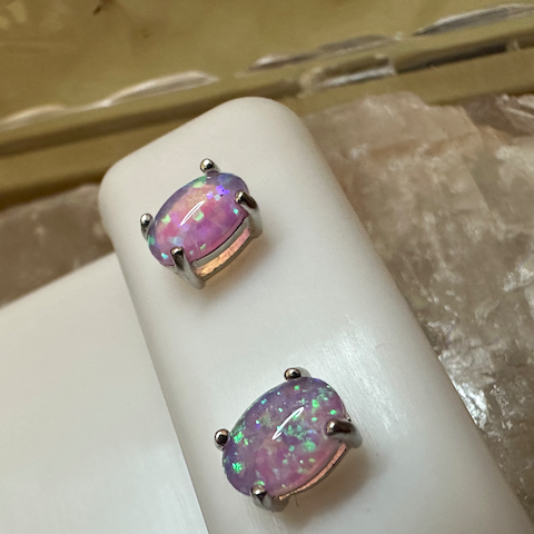 Pair of earrings with pink and purple gemstones on a white stand.
