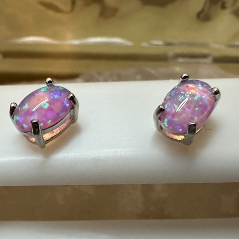 Pair of purple opal earrings on a white stand.