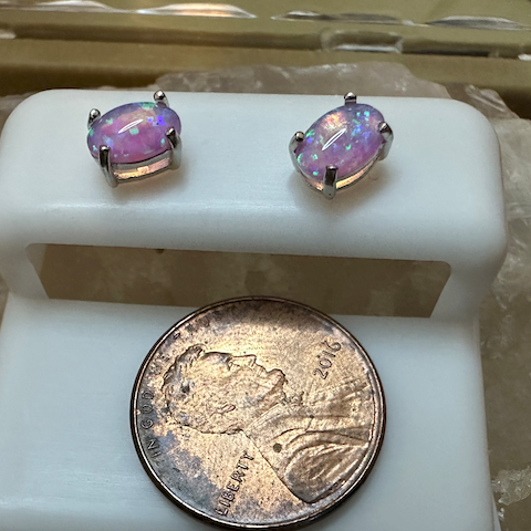 Pair of earrings with purple gemstones on a white stand next to a quarter for scale.