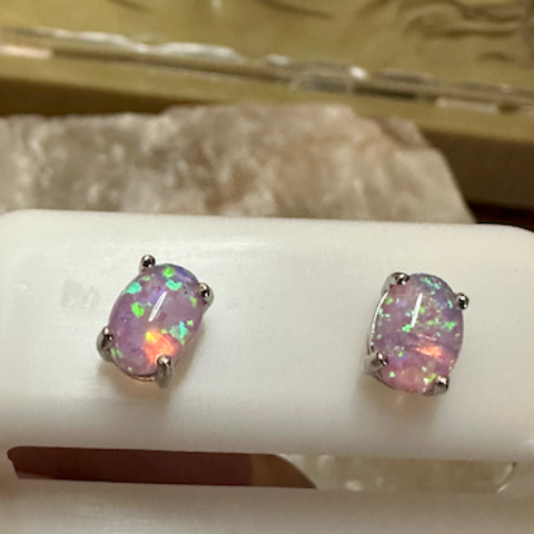 Opal stud earrings on a white stand with a decorative background