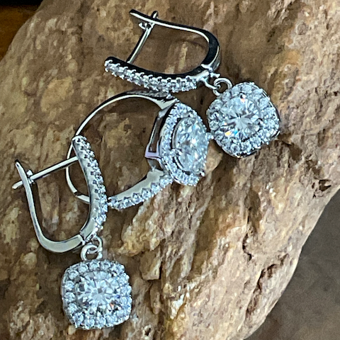 Pair of silver earrings with clear gemstones on a stone surface