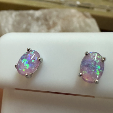 Opal stud earrings on a white card with a blurred background