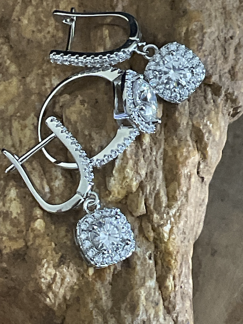 Silver earrings with clear gemstones on a textured stone background