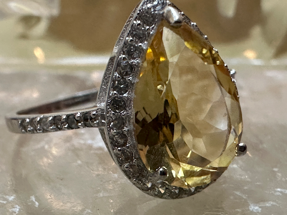 Ring with a large teardrop-shaped gemstone and smaller diamonds on a reflective surface
