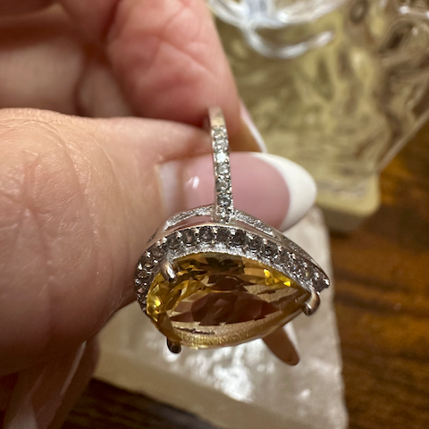 Gold ring with a large yellow gemstone held by a hand against a blurred background