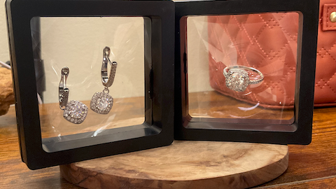 Open black jewelry display case with earrings and a ring on a wooden surface.