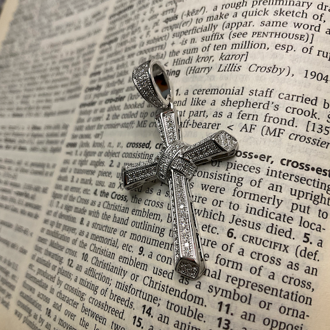 Silver cross pendant with clear stones on an open book