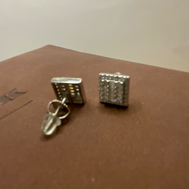 Two silver cufflinks on a brown surface with a white background