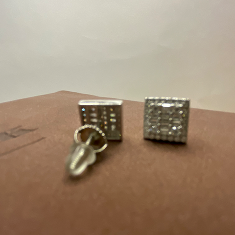Two silver cufflinks on a brown surface with a white background