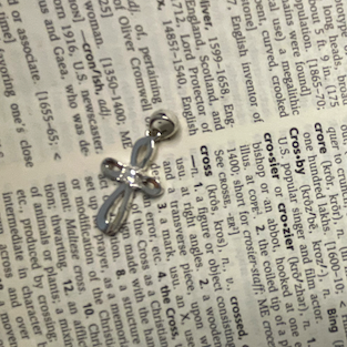 Silver cross pendant on an open book with text