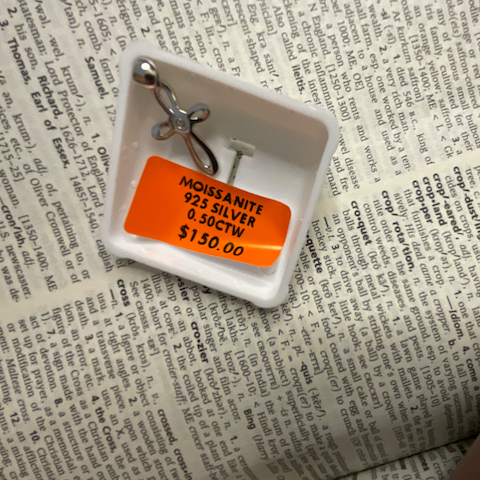 Two silver anklets on a white dish with an orange tag on a printed surface