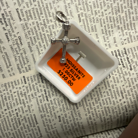 Silver cross pendant on a white dish with an orange label on a newspaper background
