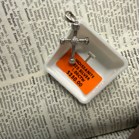 Silver cross pendant on a white dish with an orange label on a newspaper background