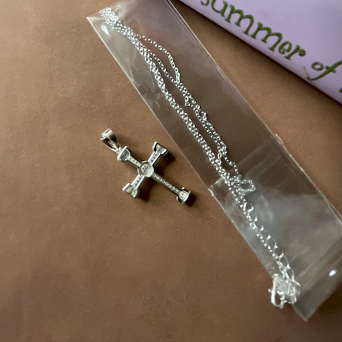 Silver cross pendant on a clear plastic stand with a book in the background