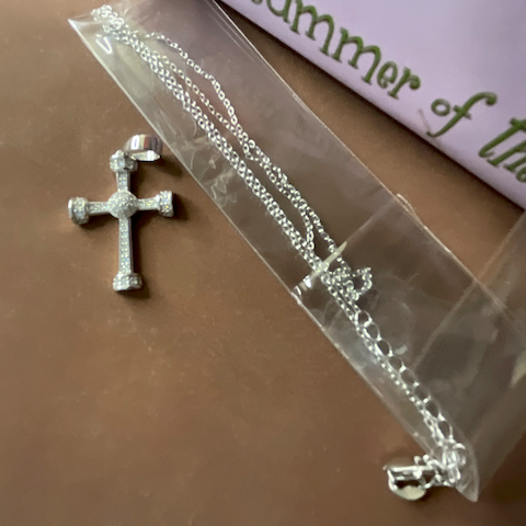 Silver cross necklace on a clear plastic bag with a book in the background