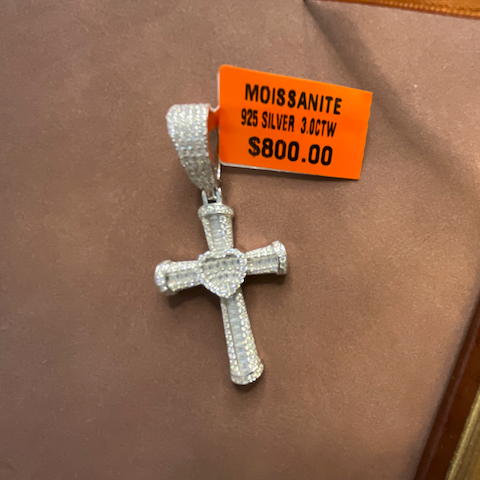 Silver cross pendant with orange tag on a brown surface