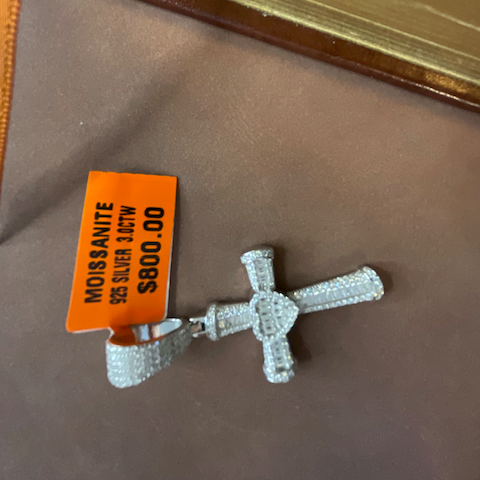Silver cross pendant with a price tag on a brown surface