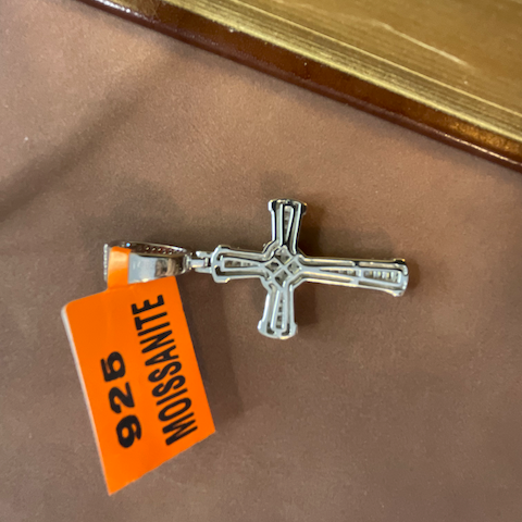 Silver cross pendant with '925' and 'MOISSANITE' tag on a brown surface