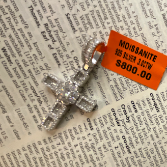 Silver cross pendant with orange tag on a printed surface
