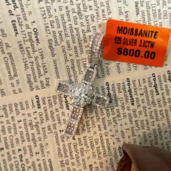 Diamond ring on a newspaper with a price tag indicating 'Moissanite VS Silver 14k $800.00'.