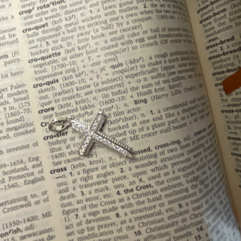 Silver cross pendant on an open book with text