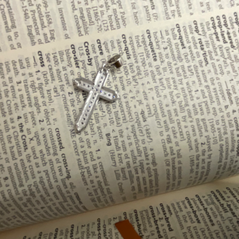 Silver cross pendant on an open book with text