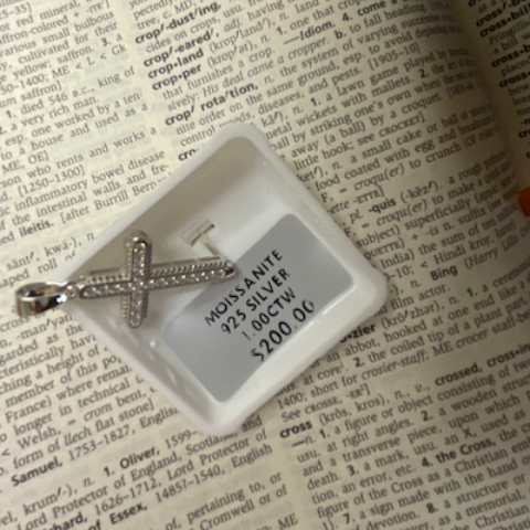 Silver cross pendant on a white card with text on a printed surface