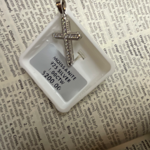 Silver cross pendant on a white card with text on a printed surface
