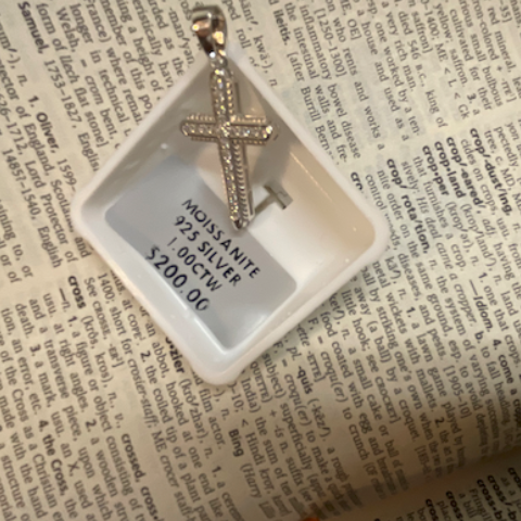 Silver cross pendant in a clear display case on a newspaper background
