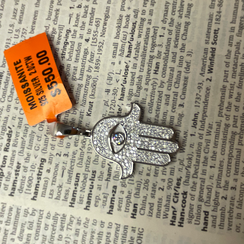Silver Hamsa hand pendant with an orange tag on a dictionary page