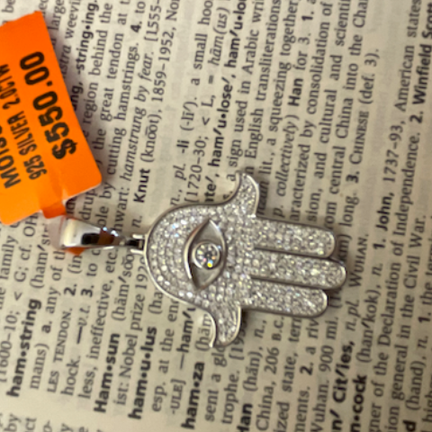 Silver Hamsa hand pendant with an orange tag on a dictionary page